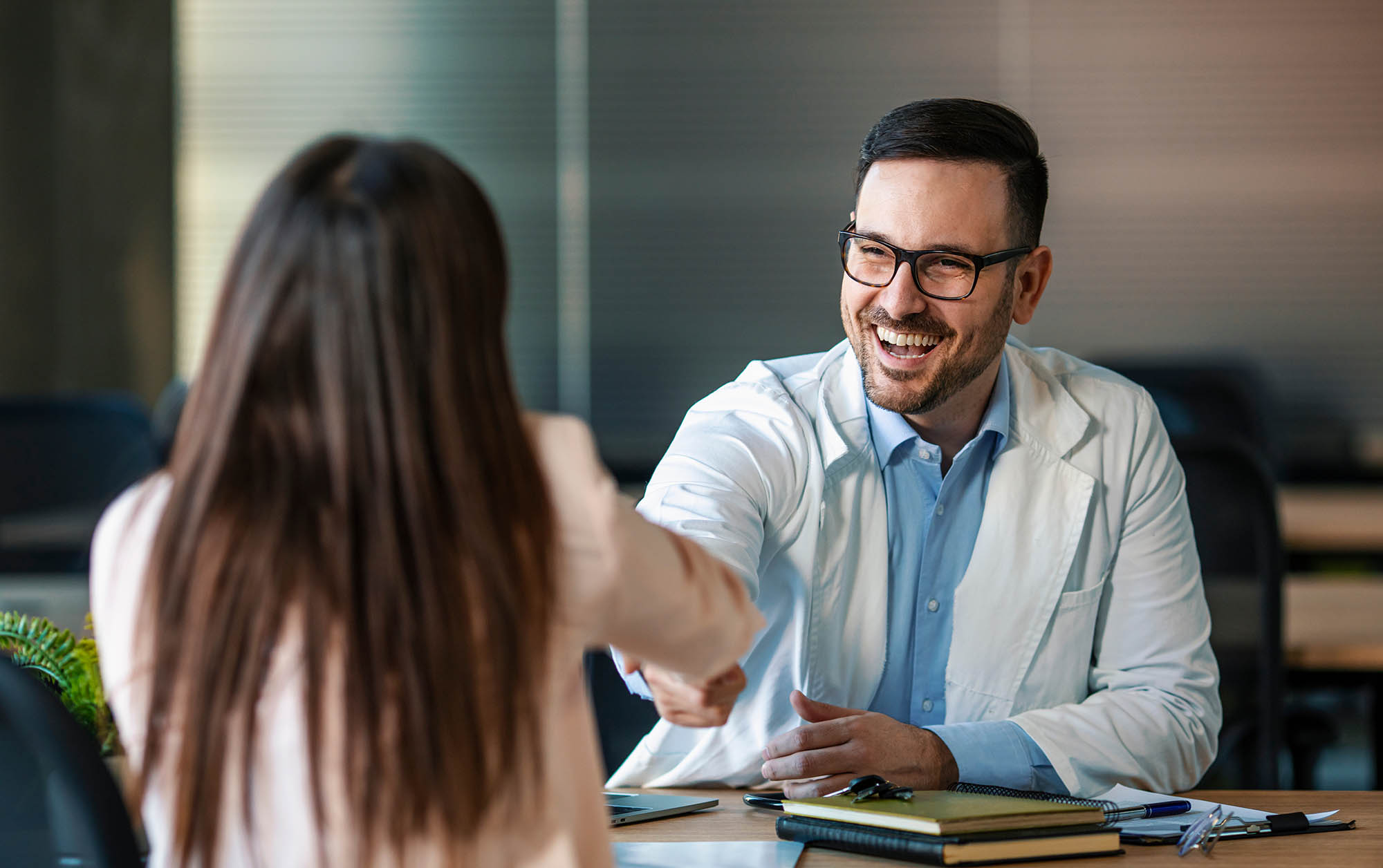 Doctor shaking hands with woman. Female patient visiting health professional. They are in hospital. Cropped shot of a handsome young male doctor and his patient shaking hands in the hospital